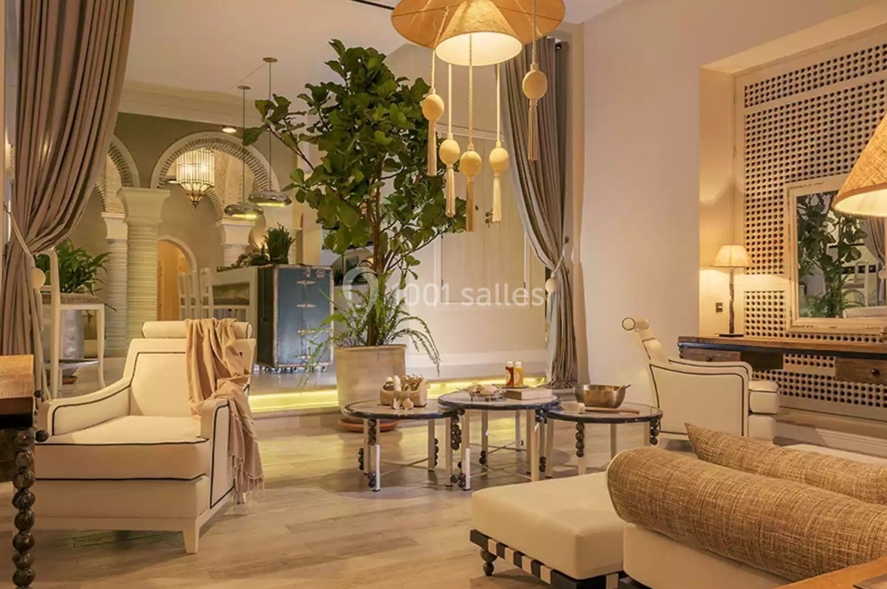 Salon élégant avec mobilier clair, luminaires suspendus, rideaux ouverts et grande plante décorative.