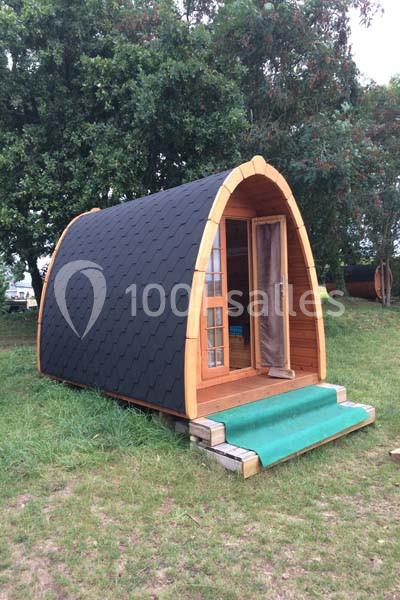 Cabane en bois en forme d'arche avec toit noir, porte vitrée et petite terrasse, située sur une pelouse.