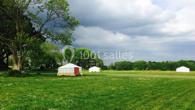 Trois yourtes blanches installées dans un grand champ verdoyant sous un ciel nuageux.