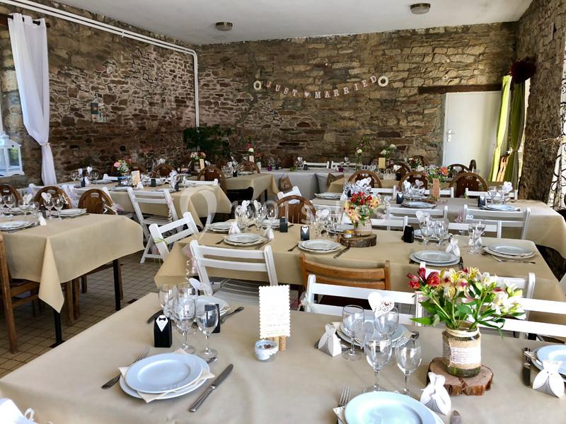 Salle de réception décorée avec des tables dressées, nappes beiges, fleurs et vaisselle pour un événement festif.