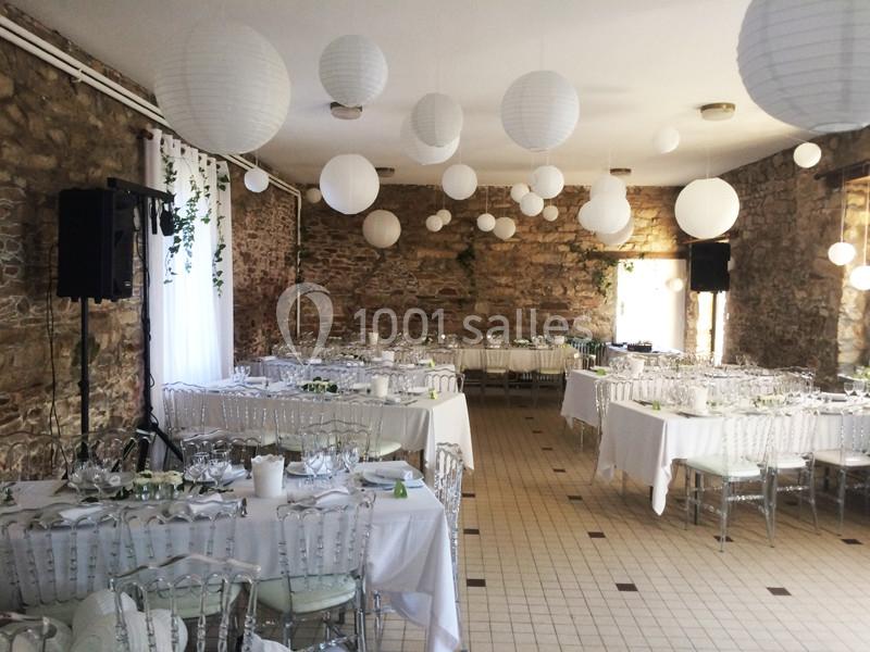 Salle de réception décorée avec des lanternes blanches suspendues, tables dressées avec nappes blanches et chaises…