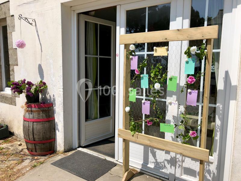 Panneau en bois décoré de fleurs et de cartes colorées devant une porte vitrée, à côté d'un tonneau fleuri.