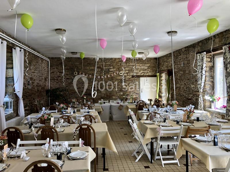Salle de réception décorée avec des ballons colorés, des tables dressées et des murs en pierre apparente.