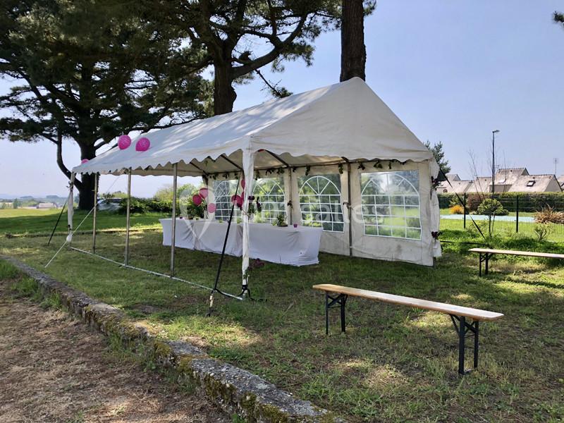 Tente blanche installée sur une pelouse avec des bancs en bois et des décorations roses suspendues.
