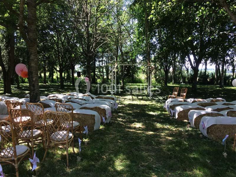 Chaises en rotin et bottes de foin décorées disposées en extérieur sous des arbres pour une cérémonie en plein air.