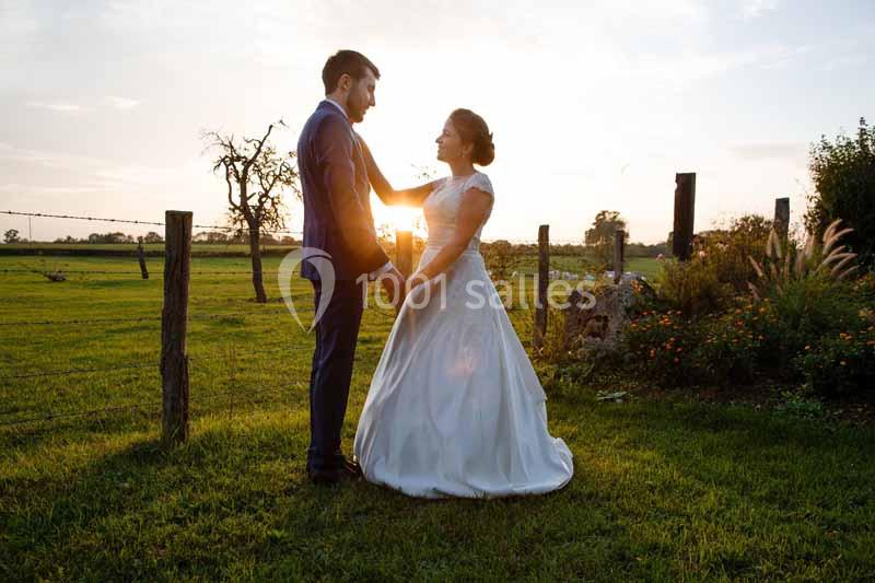 Un couple en tenue de mariage se tient debout dans un champ au coucher du soleil.