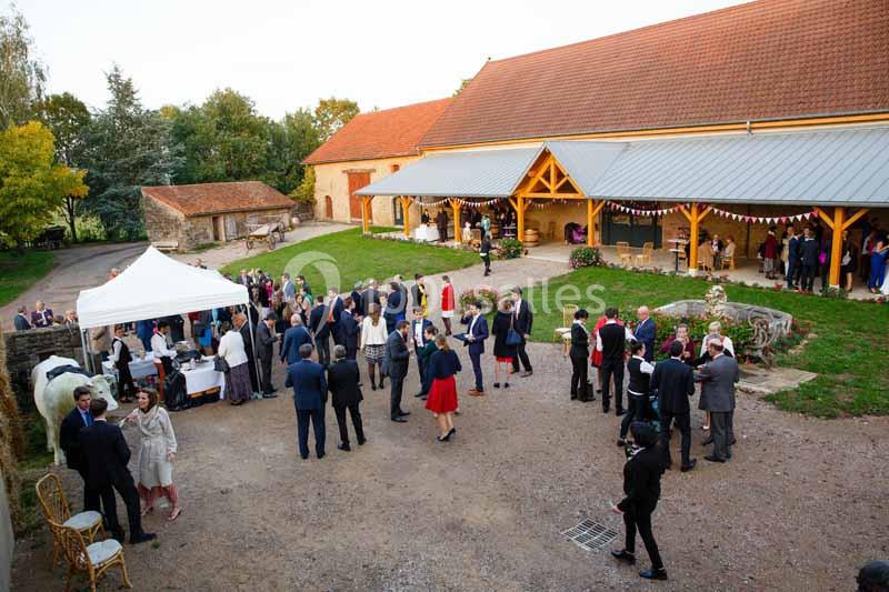 Groupe de personnes rassemblées dans la cour d'une ferme pour un événement, avec des stands et des décorations festives.