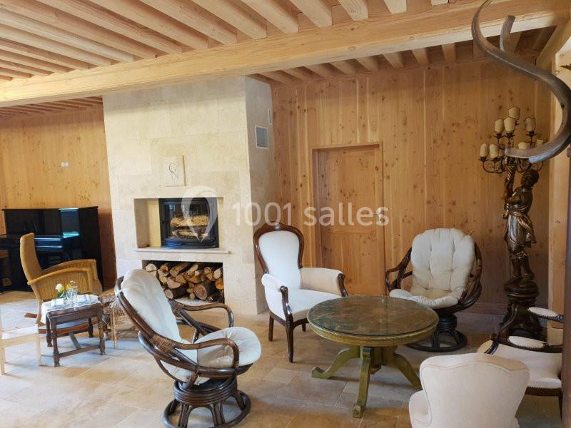 Salon chaleureux avec murs en bois, cheminée moderne, fauteuils en osier et en tissu, table ronde et décoration rustique.