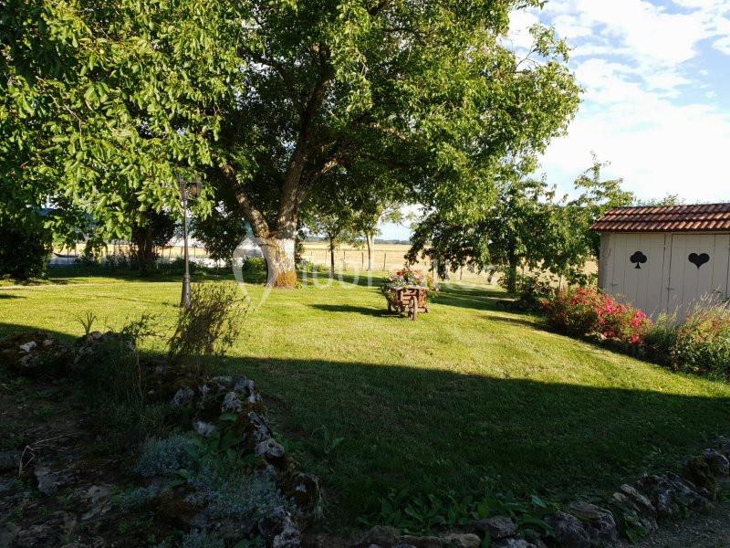 Jardin verdoyant avec arbres, pelouse, table en bois au centre et cabanon blanc décoré de cœurs en arrière-plan.