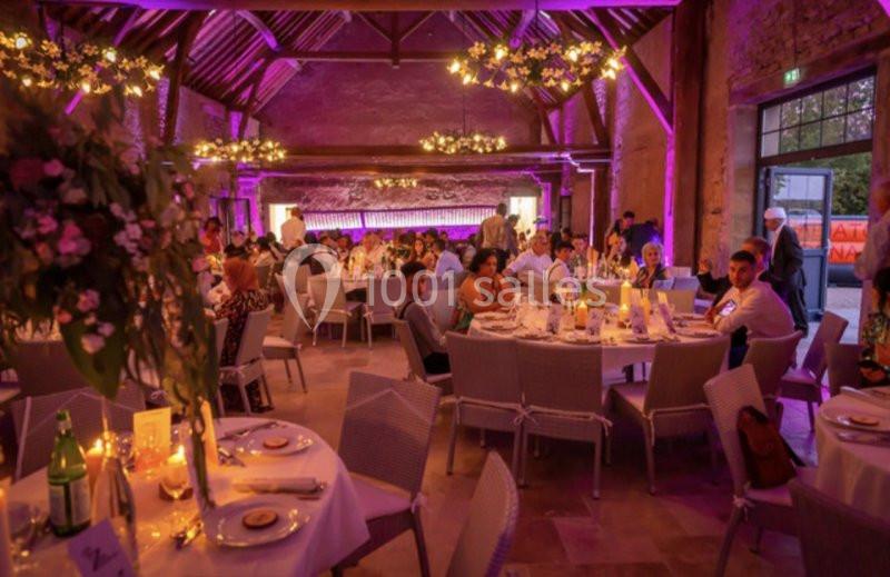 Salle de réception décorée avec des tables dressées, des invités assis et un éclairage violet chaleureux.