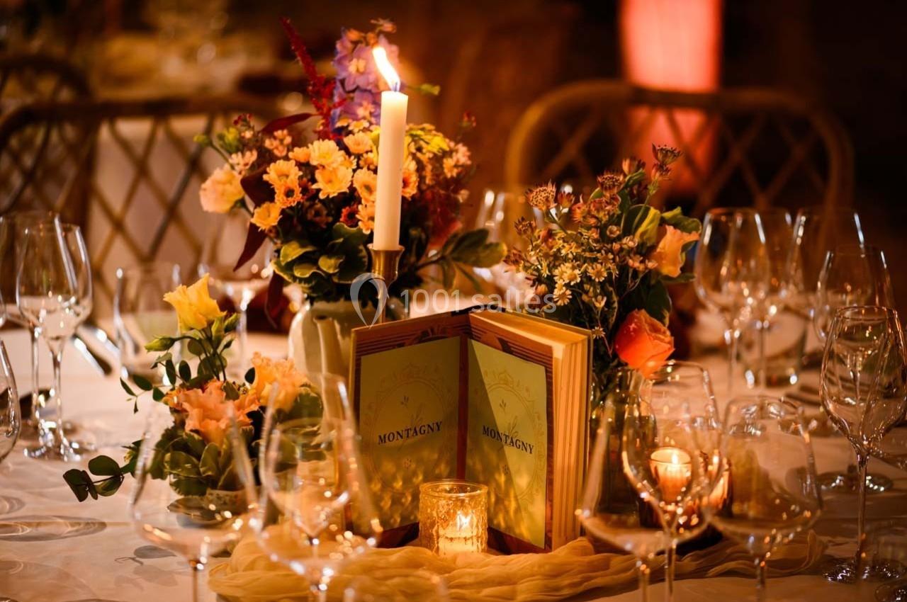 Table élégamment dressée avec bougies, fleurs colorées et menus ’Montagny’ entourés de verres à vin.