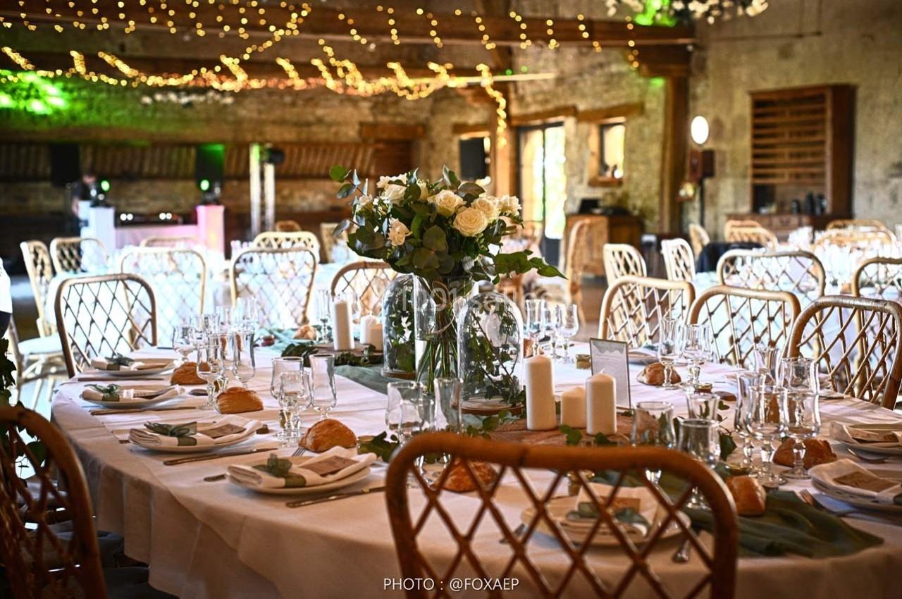 Salle de réception décorée pour un mariage, avec tables dressées, chandelles, fleurs et guirlandes lumineuses suspendues.