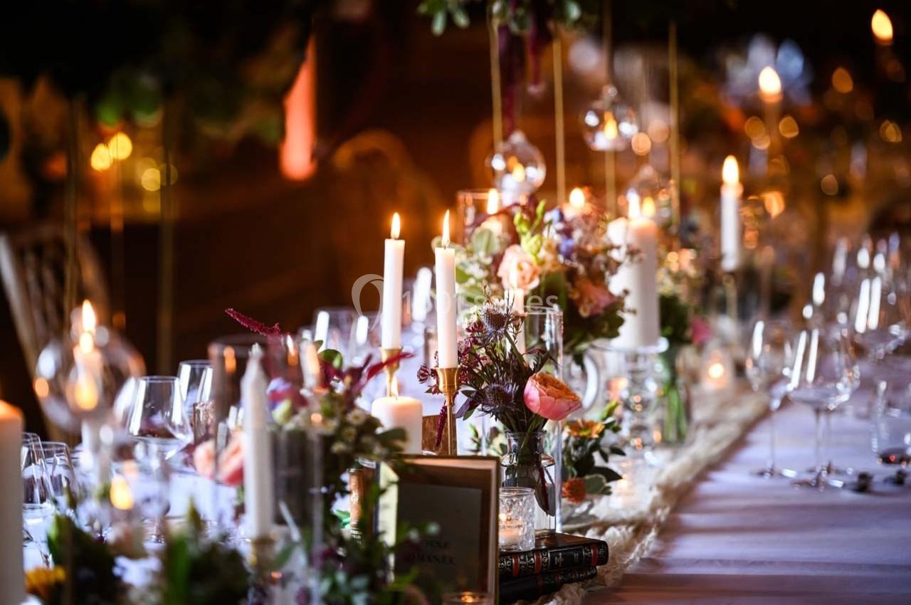 Table élégamment décorée avec bougies allumées, fleurs colorées et verres disposés pour un dîner festif.