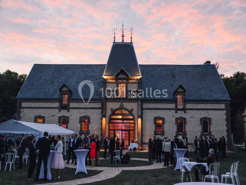Groupe de personnes rassemblées devant un bâtiment ancien avec toit en ardoise, au coucher du soleil.