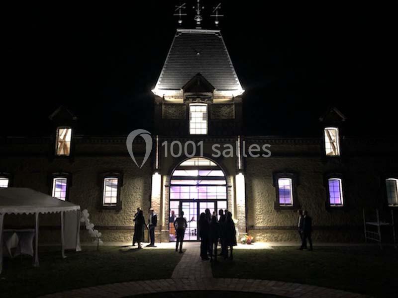 Façade d'un bâtiment éclairé de nuit, avec des silhouettes de personnes devant l'entrée principale.