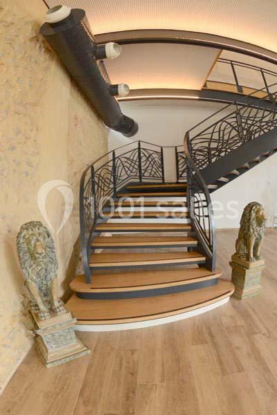 Escalier en bois avec garde-corps en métal, encadré par deux statues de lions sur des socles, dans un intérieur moderne.