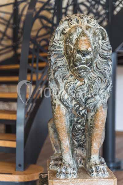 Statue de lion en pierre devant un escalier en métal et bois dans un intérieur lumineux.
