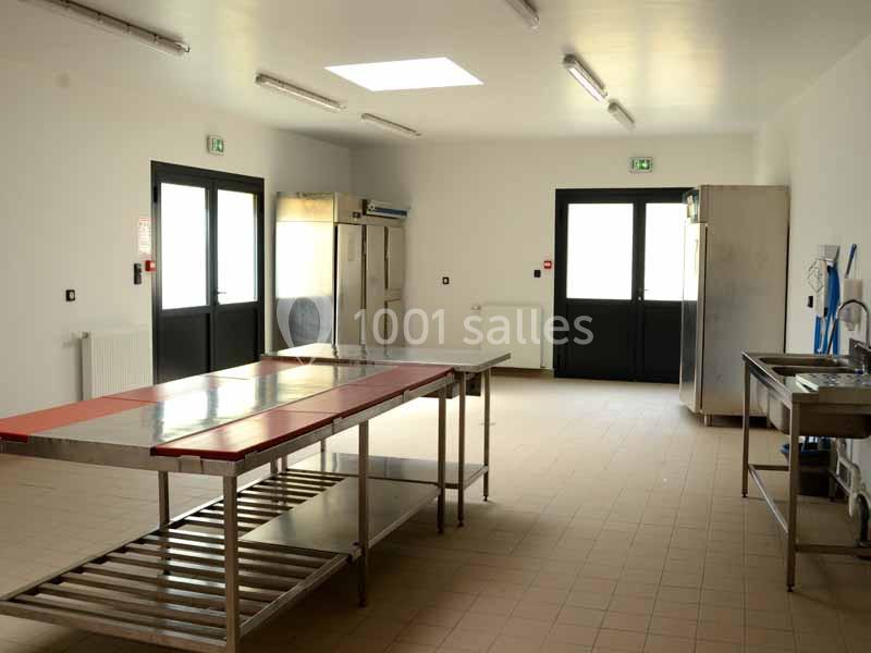 Cuisine professionnelle vide avec plans de travail en inox, équipements de rangement et éclairage naturel par une fenêtre de…