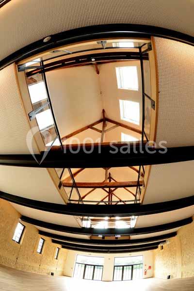 Plafond d'une salle avec poutres apparentes, verrière centrale et murs en pierre claire.