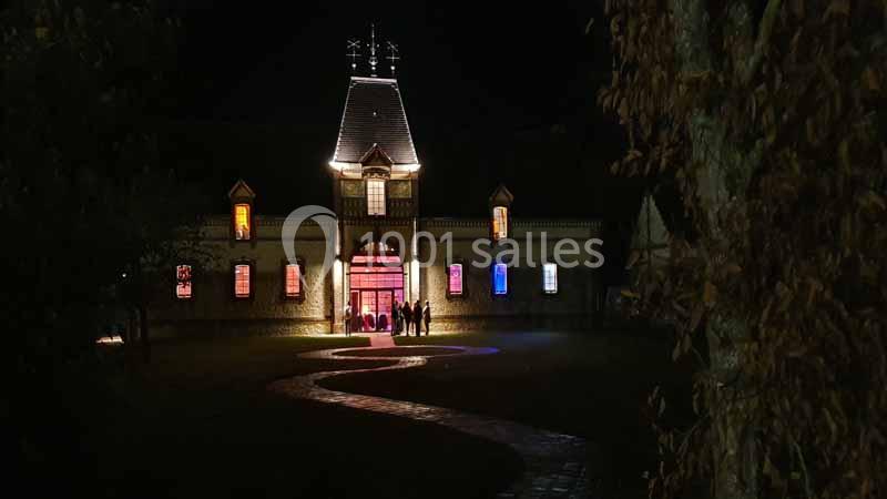 Façade d'un bâtiment illuminé la nuit, avec un chemin pavé menant à une entrée éclairée.