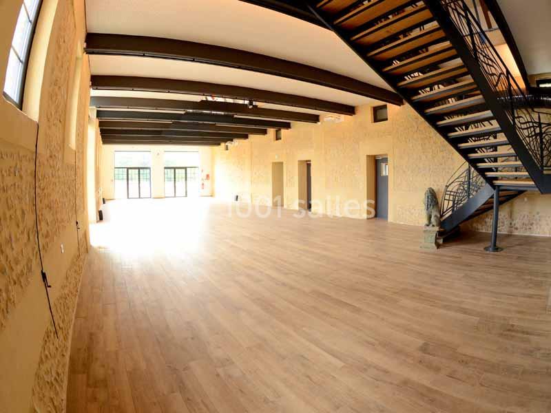 Salle spacieuse avec parquet en bois, murs en pierre apparente, poutres métalliques et escalier moderne en métal.