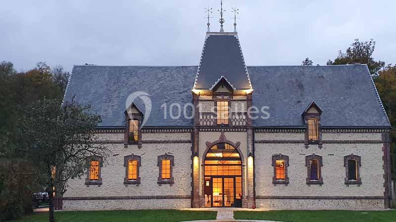 Façade d'un bâtiment en briques et pierre avec toit en ardoise, éclairé à la tombée de la nuit.