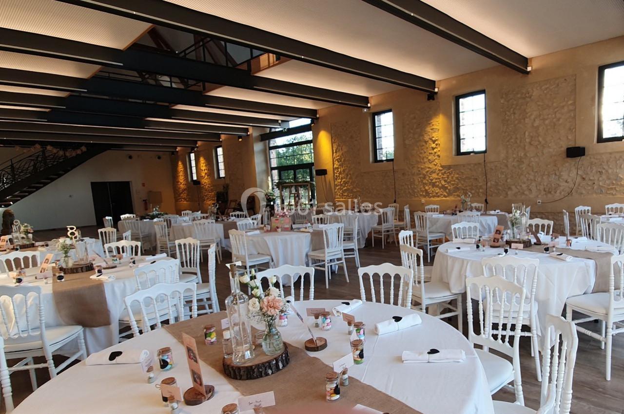Salle de réception lumineuse avec tables rondes décorées de nappes blanches, chaises assorties et centres de table floraux.