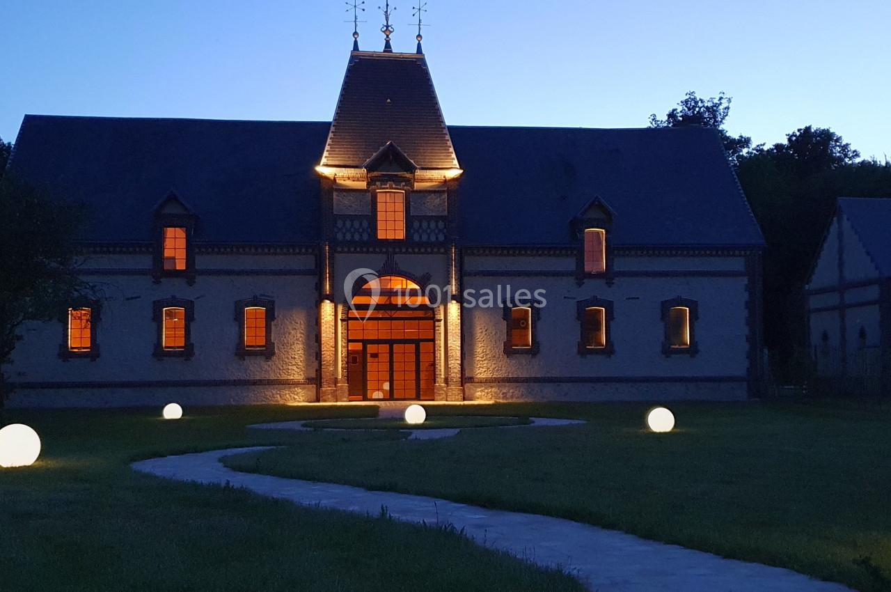 Bâtiment en briques éclairé à la tombée de la nuit, avec un chemin bordé de sphères lumineuses dans un jardin.