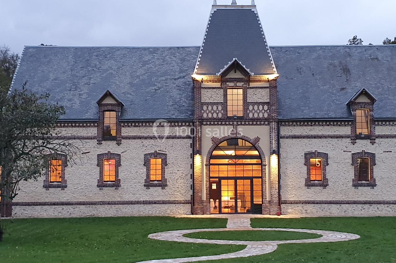 Façade d'un bâtiment en briques avec toit en ardoise, éclairé à la tombée de la nuit, entouré de pelouse.