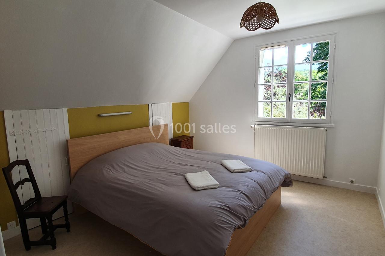 Chambre lumineuse avec un lit double, deux serviettes pliées, une fenêtre donnant sur un jardin et un fauteuil en bois.