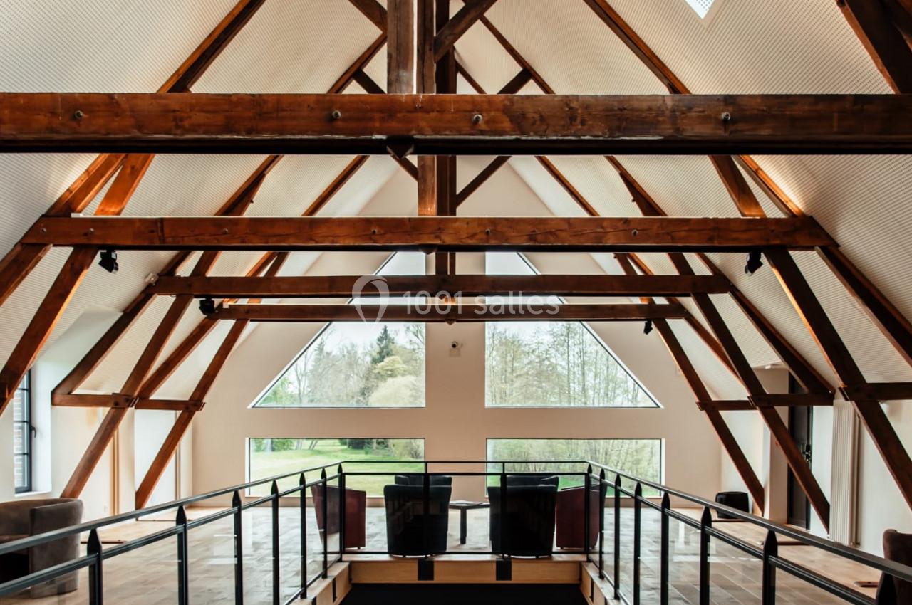 Intérieur d'un bâtiment avec une charpente en bois apparente, mezzanine et grandes fenêtres laissant entrer la lumière…