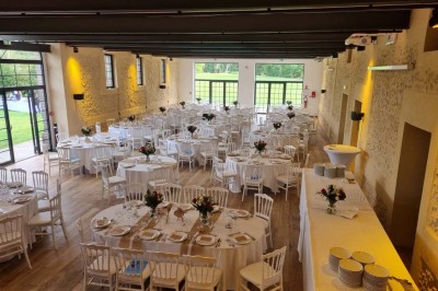 Salle de réception décorée avec des tables rondes, nappes blanches, chaises blanches et centres de table fleuris.