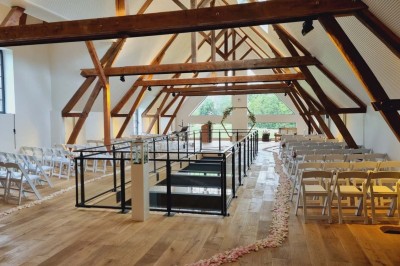 Salle de réception décorée avec des tables rondes, nappes blanches, chaises blanches et centres de table fleuris.