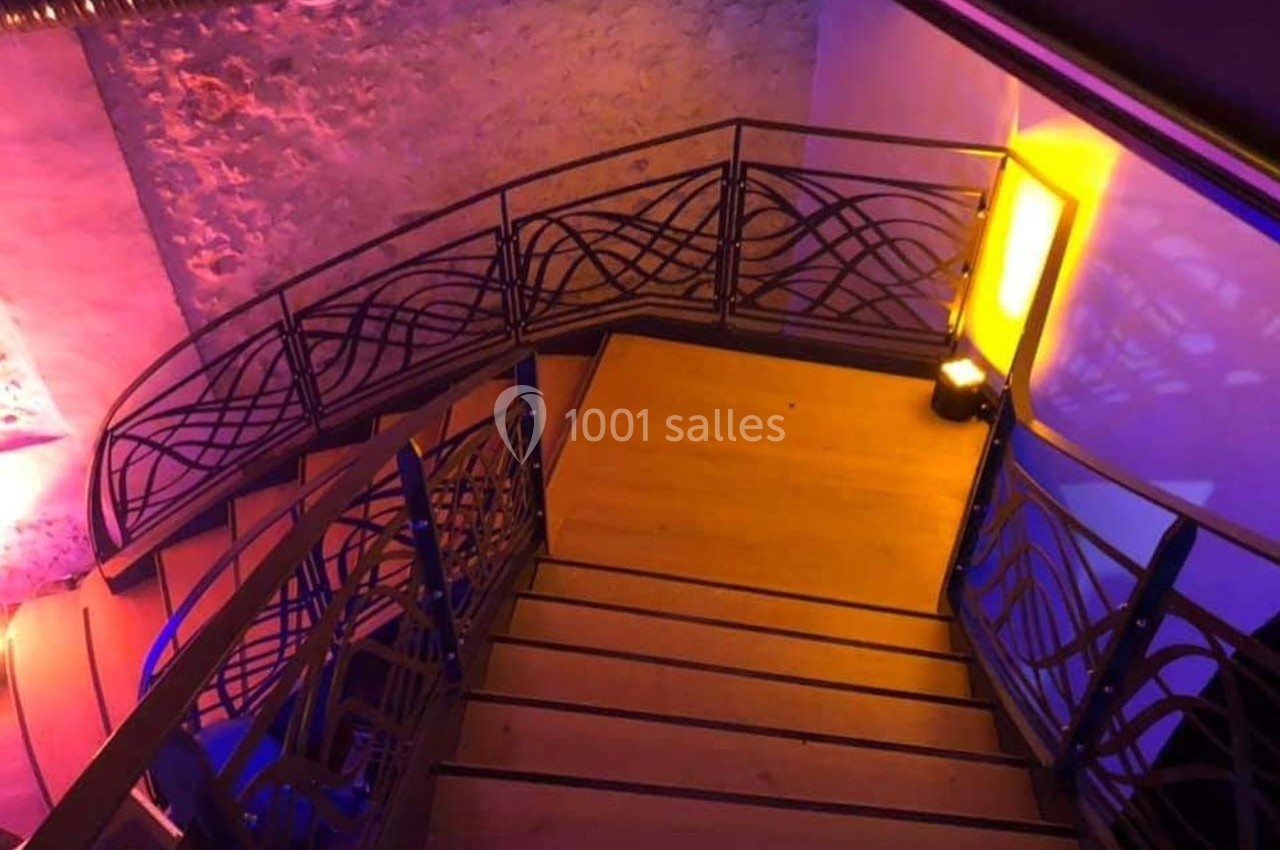Escalier en bois avec rambardes en métal décoratif, éclairé par des lumières colorées dans un intérieur moderne.