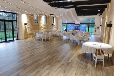 Salle de réception décorée avec des tables rondes, nappes blanches, chaises blanches et centres de table fleuris.