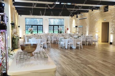 Salle de réception décorée avec des tables rondes, nappes blanches, chaises blanches et centres de table fleuris.