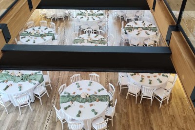 Salle de réception décorée avec des tables rondes, nappes blanches, chaises blanches et centres de table fleuris.