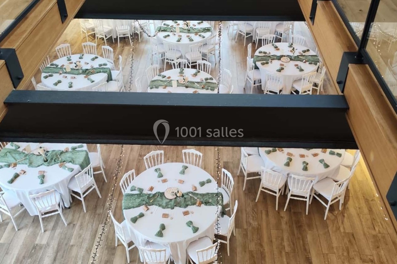 Vue plongeante sur une salle de réception avec des tables rondes décorées de nappes vertes et de chaises blanches.