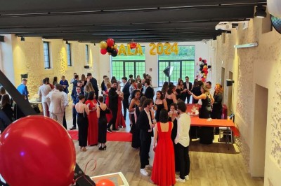 Salle de réception décorée avec des tables rondes, nappes blanches, chaises blanches et centres de table fleuris.