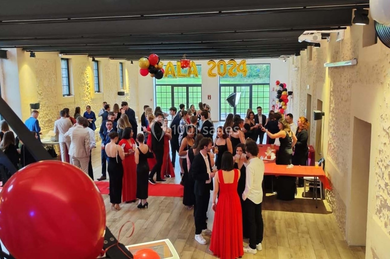 Salle décorée pour un gala, avec des invités en tenue de soirée discutant autour de tables et d'un buffet.