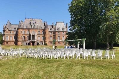 Salle de réception décorée avec des tables rondes, nappes blanches, chaises blanches et centres de table fleuris.
