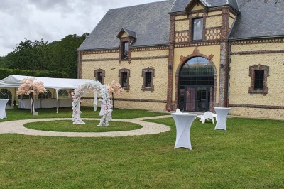 Salle de réception décorée avec des tables rondes, nappes blanches, chaises blanches et centres de table fleuris.