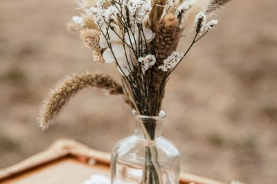 Salle de réception décorée avec des tables rondes, nappes blanches, chaises blanches et centres de table fleuris.