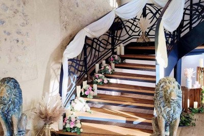 Salle de réception décorée avec des tables rondes, nappes blanches, chaises blanches et centres de table fleuris.