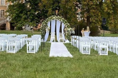 Salle de réception décorée avec des tables rondes, nappes blanches, chaises blanches et centres de table fleuris.