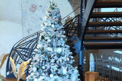 Salle de réception décorée avec des tables rondes, nappes blanches, chaises blanches et centres de table fleuris.