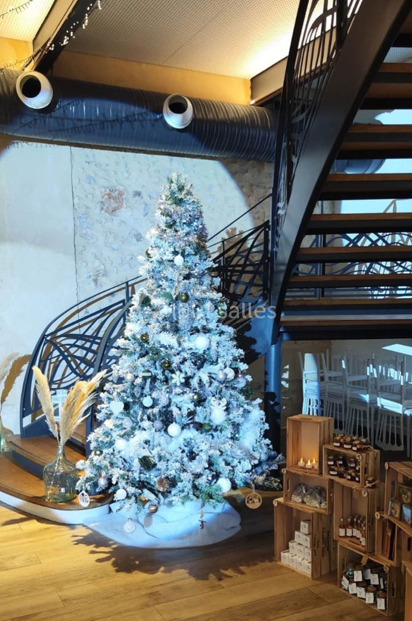 Sapin de Noël décoré en blanc et argent, placé près d'un escalier métallique dans un espace intérieur lumineux.