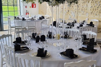 Salle de réception décorée avec des tables rondes, nappes blanches, chaises blanches et centres de table fleuris.