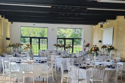 Salle de réception décorée avec des tables rondes, nappes blanches, chaises blanches et centres de table fleuris.