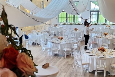 Salle de réception décorée avec des tables rondes, nappes blanches, chaises blanches et centres de table fleuris.
